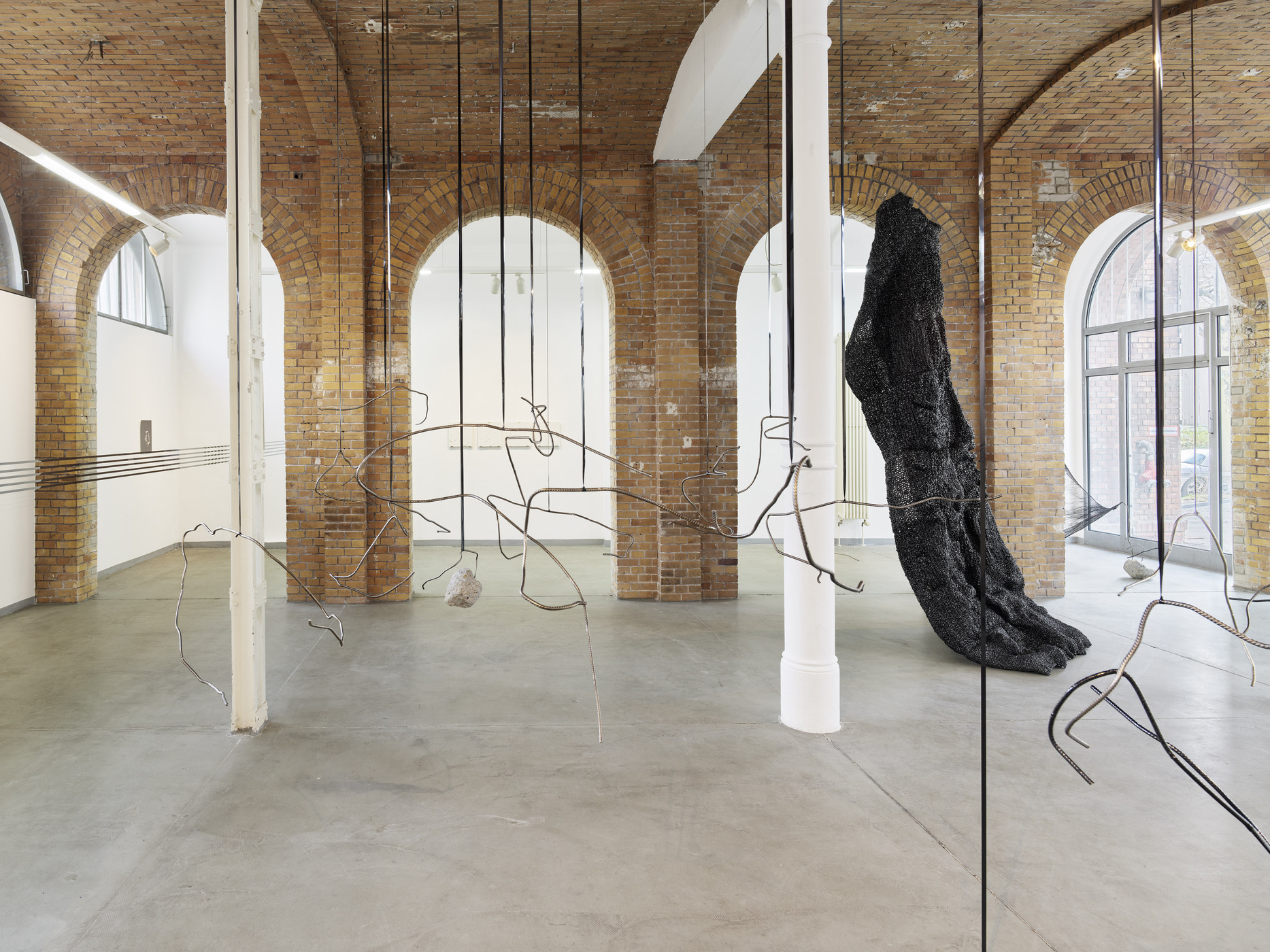 Installation view by Vanessa Enríquez with suspended wire sculpture and black monumental structure.