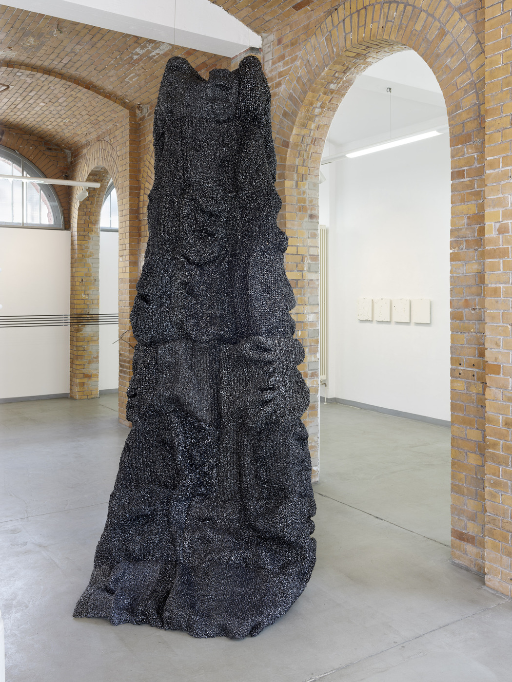 Black textured sculptural installation by Vanessa Enríquez framed by brick arches.
