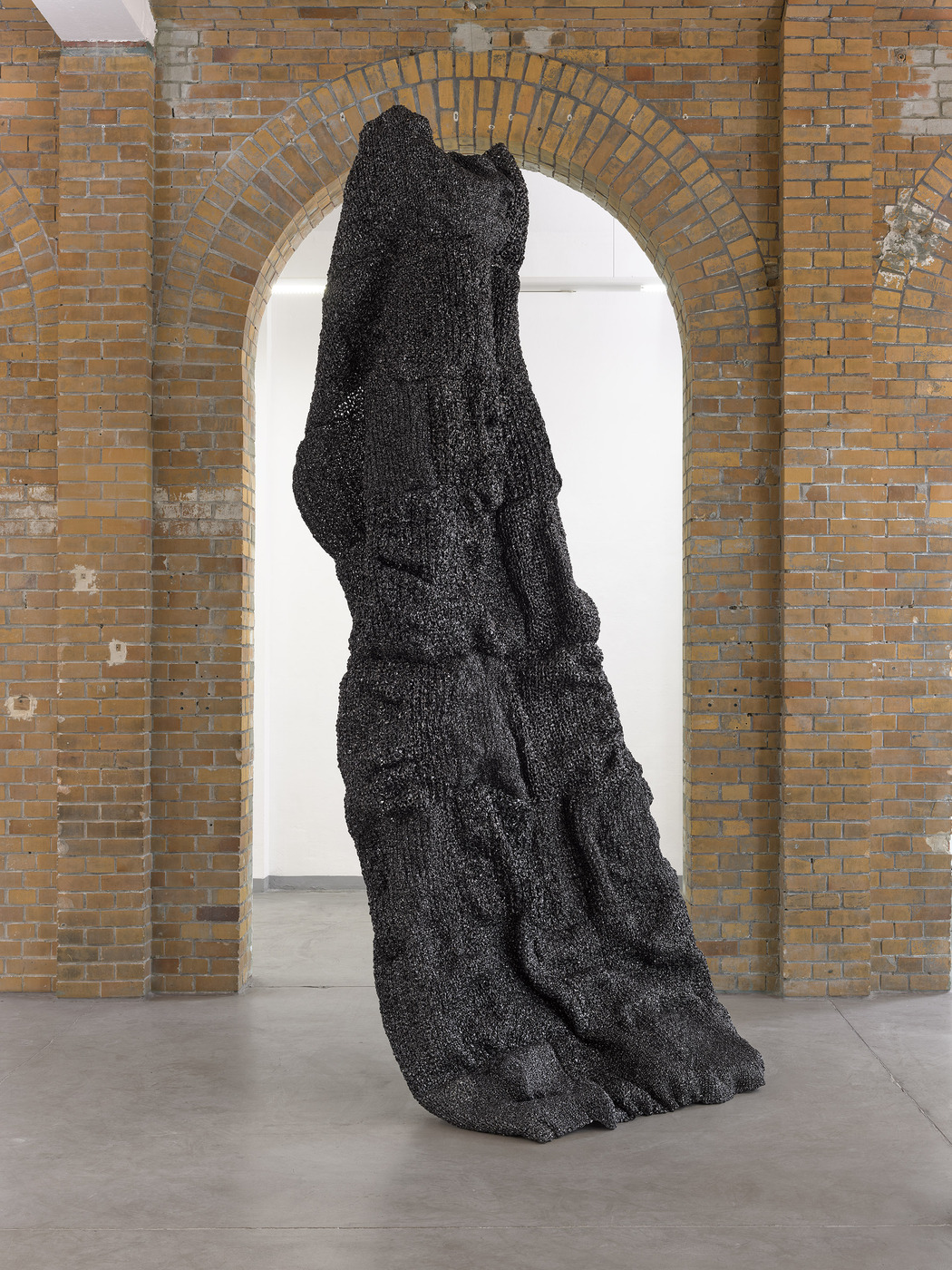 Side view of monumental black sculpture by Vanessa Enríquez in gallery space.