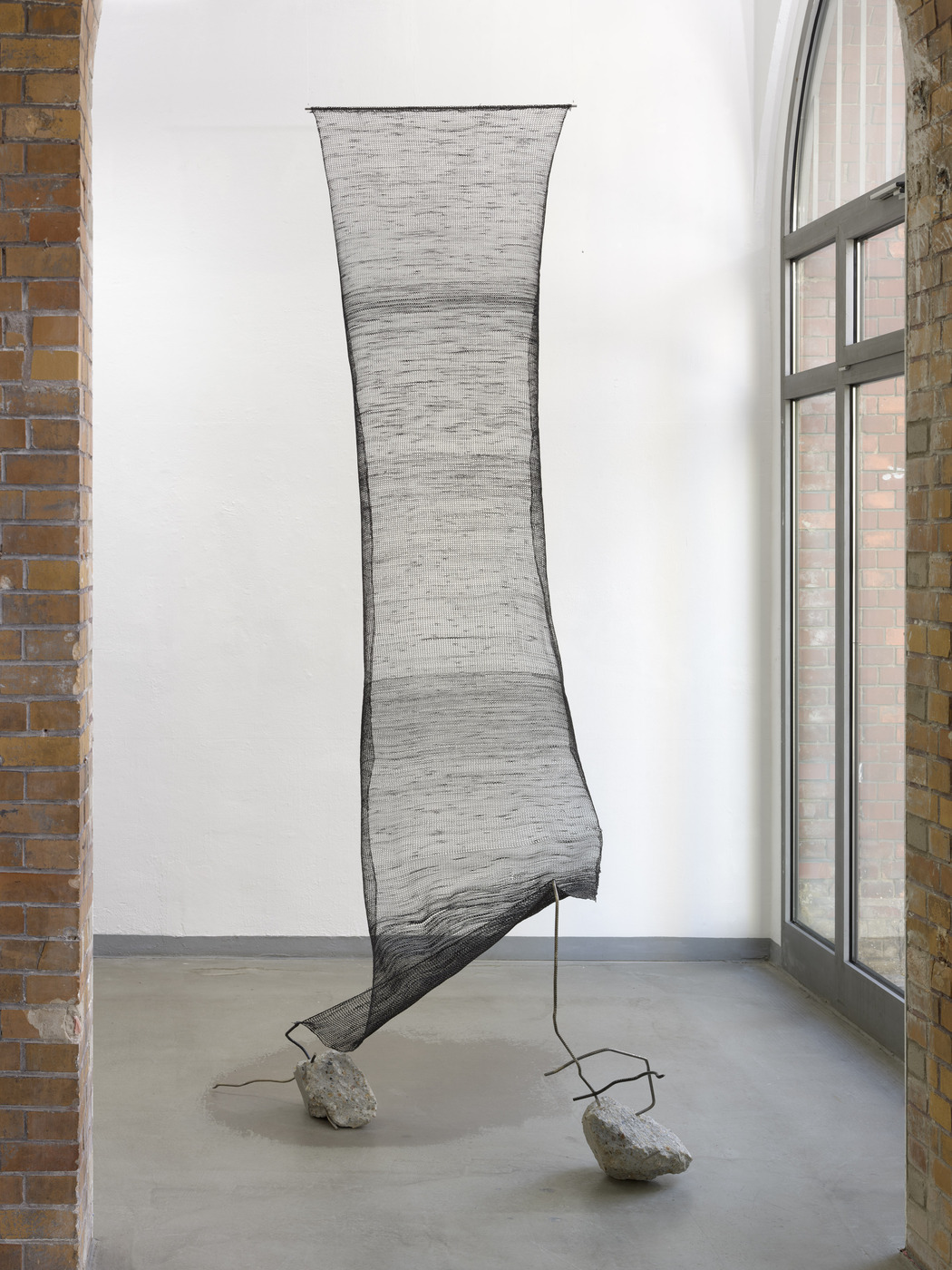 Suspended mesh installation by Vanessa Enríquez displayed in industrial gallery space.