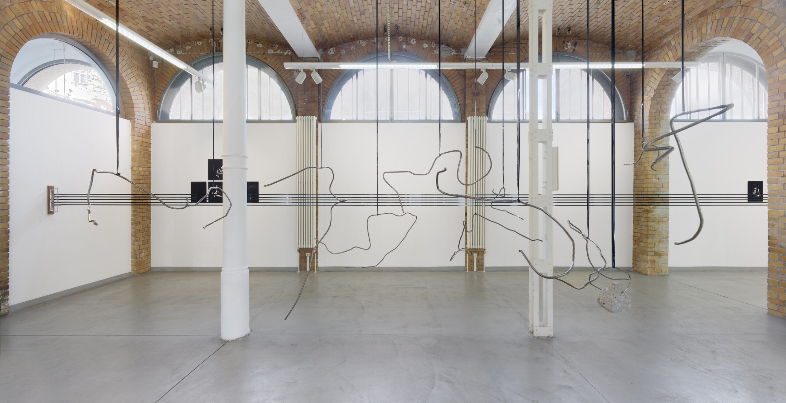 Panoramic installation view by Vanessa Enríquez with suspended sculptures and photographic works.